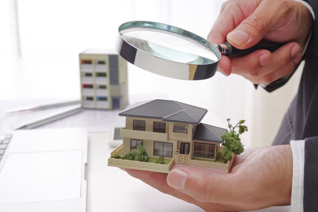 虫眼鏡で家の模型を見る人物